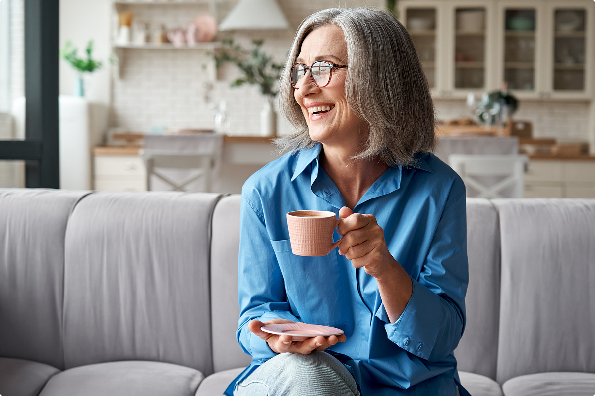Donna sorridente che beve una tazza di tè seduta sul divano di casa.