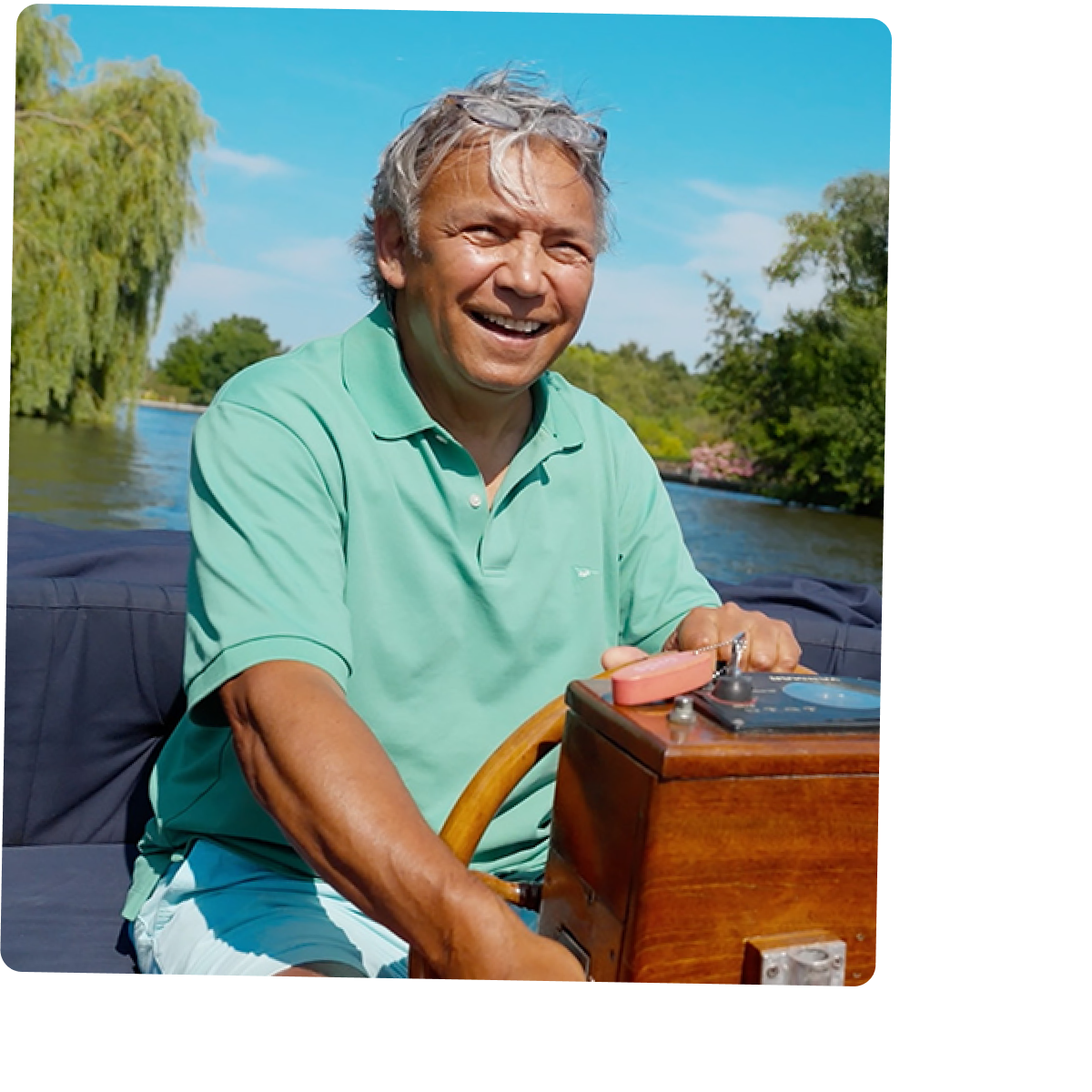 Een man bestuurt een kleine motorboot op een rivier, met bomen op de achtergrond.